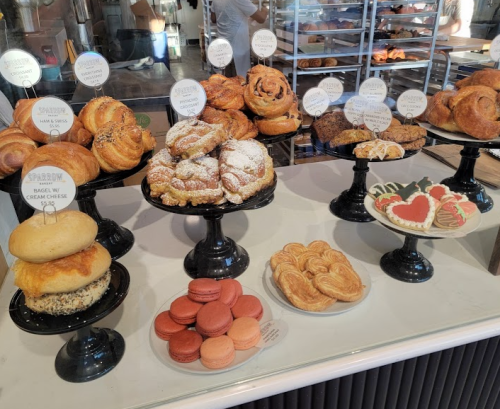 A display of various baked goods, including pastries, cookies, and macarons on black stands in a bakery.
