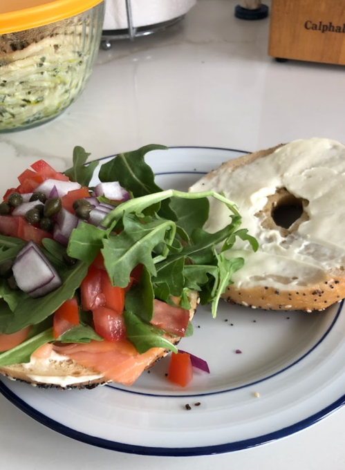 A bagel half topped with cream cheese, smoked salmon, arugula, tomatoes, red onion, and capers on a plate.