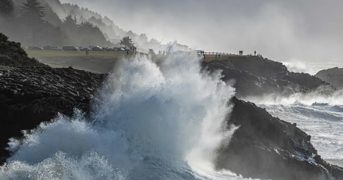 Waves crash against rocky cliffs under a misty sky, with trees and distant figures in the background.