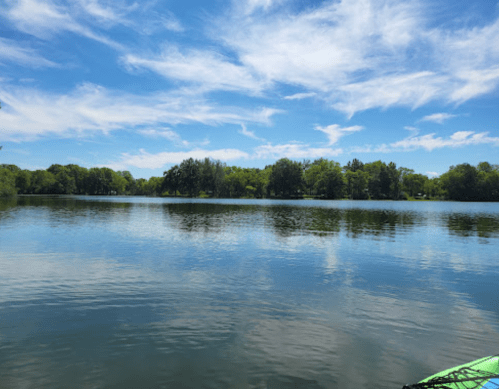 A serene lake reflecting blue skies and lush green trees, with gentle ripples on the water's surface.