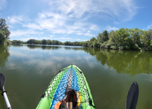 A kayak on calm water, surrounded by lush greenery and a clear blue sky.