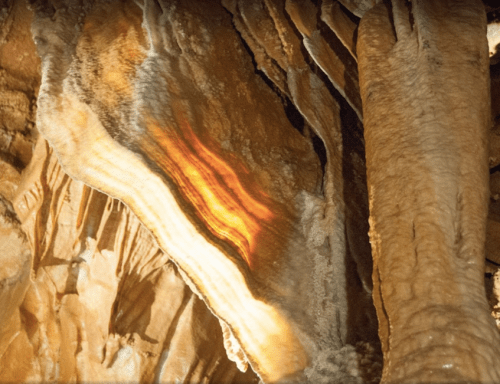 Close-up of a cave wall featuring layered rock formations with a warm orange glow.