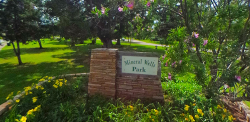 Sign for Mineral Wells Park surrounded by greenery and colorful flowers.