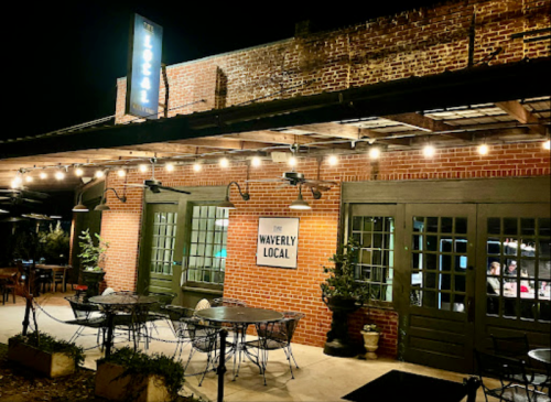 A cozy restaurant exterior at night, featuring brick walls, string lights, and outdoor seating.
