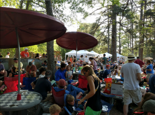 A crowded outdoor gathering under umbrellas, with people socializing and enjoying food in a park setting.