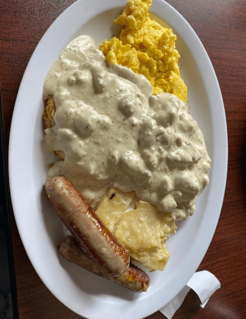 A plate of breakfast featuring scrambled eggs, sausage links, and biscuits smothered in creamy gravy.