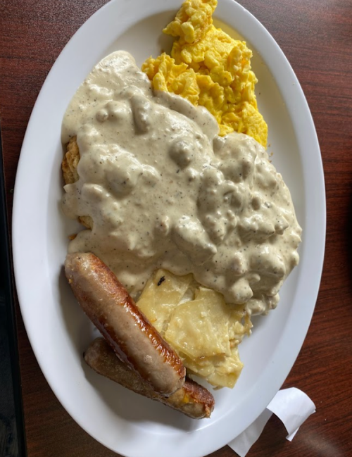 A plate of breakfast featuring scrambled eggs, sausage links, and biscuits smothered in creamy gravy.