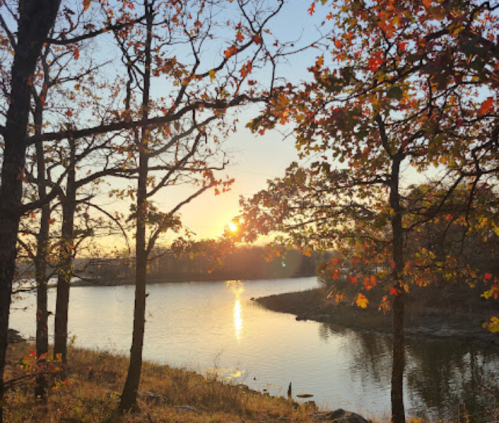 A serene sunset over a calm lake, framed by trees with autumn leaves in warm colors.
