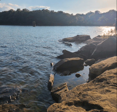 A serene lakeside view with rocky shorelines and gentle waves under a clear sky.