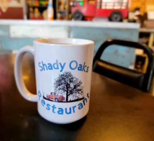 A white coffee mug with "Shady Oaks Restaurant" and an image of a tree and a vintage truck.