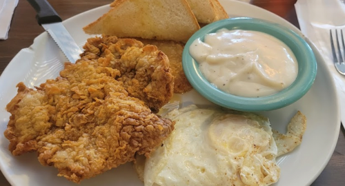 A plate with fried chicken, a fried egg, toast, and a small bowl of creamy sauce.