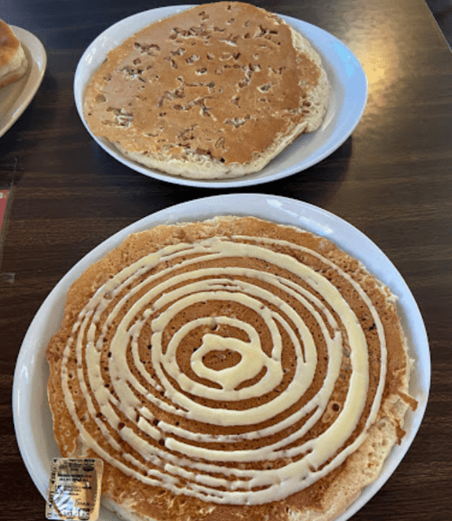 Two plates of pancakes: one with a swirl of icing and the other topped with nuts, both on a wooden table.