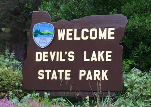 Welcome sign for Devil's Lake State Park in Oregon, featuring the state parks logo and surrounded by greenery.