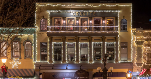 A festive building adorned with string lights, showcasing holiday decorations and storefronts below.