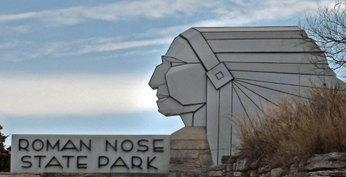 Sign for Roman Nose State Park featuring a stylized Native American head silhouette against a blue sky.