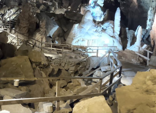 A winding pathway through a cave with rock formations and illuminated stalactites.