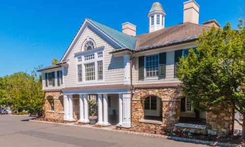 A large, elegant building with a stone base, white columns, and green shutters under a clear blue sky.