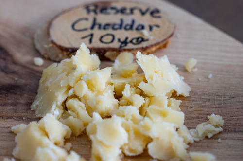 Crumbled pieces of 10-year aged cheddar cheese on a wooden board with a label.
