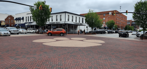 A brick intersection featuring a large paw print design, with shops and people in the background under a cloudy sky.