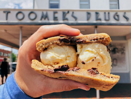 A hand holds a cookie sandwich filled with two scoops of vanilla ice cream outside Toomer's Drugs.