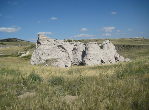 A large, white rock formation surrounded by green grass under a blue sky with scattered clouds.