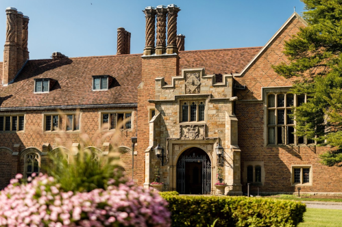 A grand brick mansion with intricate architectural details, surrounded by lush greenery and colorful flowers.