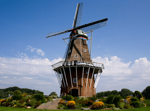 A traditional windmill surrounded by colorful flowers and greenery under a clear blue sky.