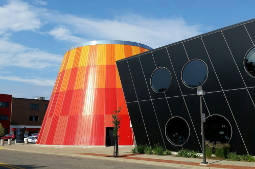 Colorful cylindrical building with red and orange stripes next to a modern black structure with circular windows.