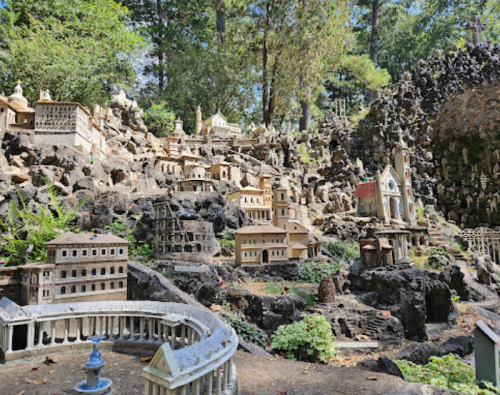 A miniature village with detailed buildings set among rocky terrain and greenery, surrounded by trees.