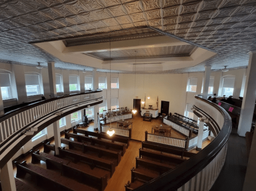 Interior view of a church with a circular balcony, wooden pews, and a bright, open space.