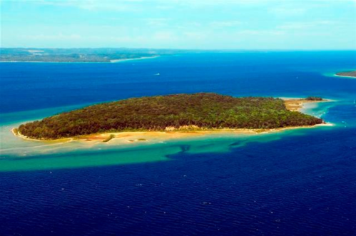 Aerial view of a lush green island surrounded by blue waters and sandy shores.