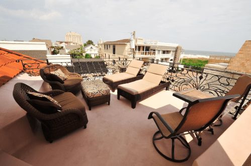 A rooftop terrace with lounge chairs, a small table, and a view of the ocean and nearby buildings.