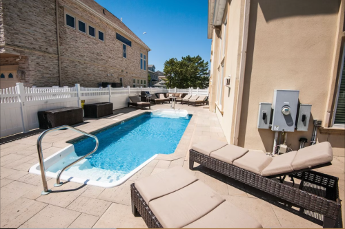 A sunny backyard with a small pool, lounge chairs, and a white fence surrounding the area.