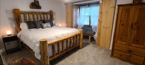 Cozy bedroom featuring a log bed, wooden furniture, and natural light from a window with sheer curtains.