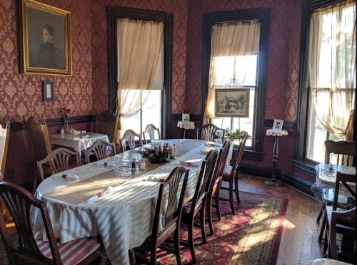 A dining room with a long table set for a meal, surrounded by elegant decor and large windows with drapes.
