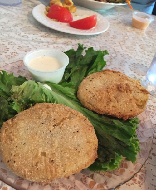 Two golden-brown fried patties on a bed of lettuce, served with a small cup of dipping sauce.