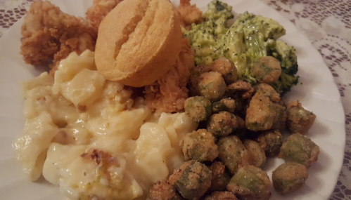 A plate of fried chicken, cornbread muffin, macaroni and cheese, broccoli, and fried okra on a lace tablecloth.