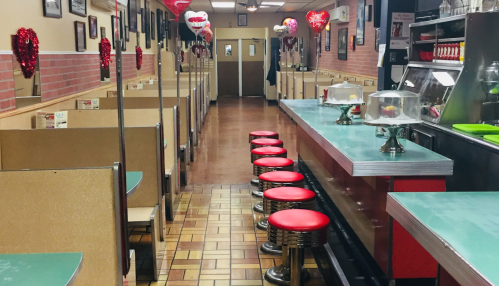 A retro diner interior with red stools, booths, and Valentine's decorations along the walls.