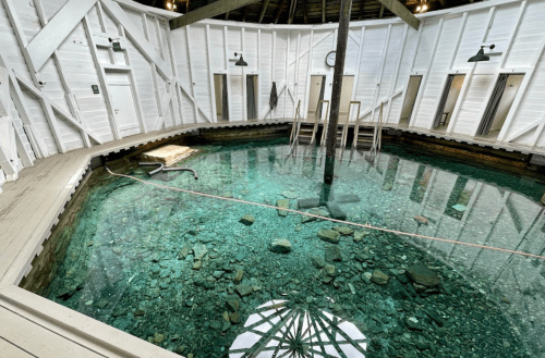 A spacious, white-walled room with a clear, shallow pool of water and a central wooden support pillar.