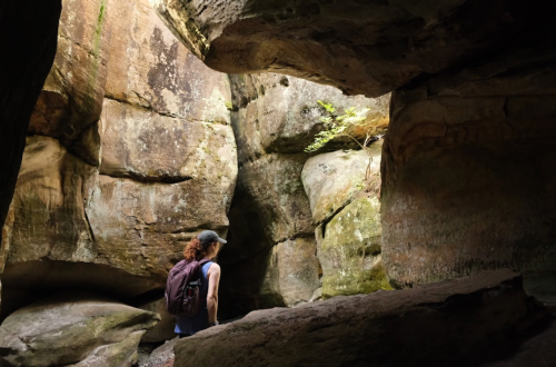 A person with a backpack explores a rocky cave, surrounded by large stone formations and soft natural light.