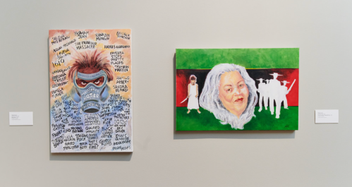 Two paintings on a wall: one features a masked figure with text, the other depicts a woman against a green background.