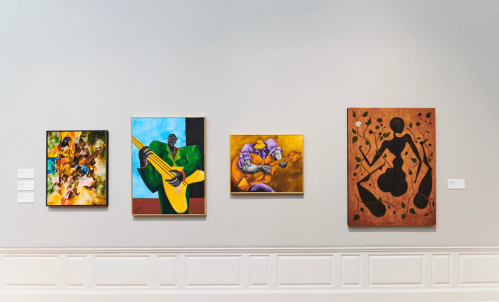 Four colorful paintings depicting musicians and dancers, displayed on a gallery wall with labels underneath.
