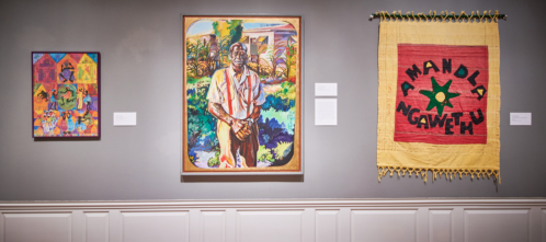 Three artworks displayed on a gallery wall: a colorful painting, a portrait, and a textile with bold text.