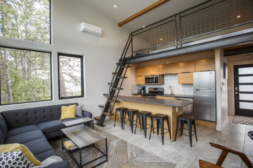 Modern open-concept living space with a kitchen, dining area, and a cozy seating area featuring large windows and a loft.