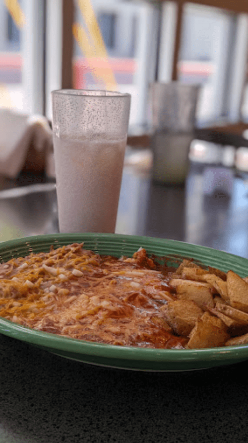 A plate of cheesy enchiladas with a side of crispy potatoes, accompanied by a frosty drink in a glass.