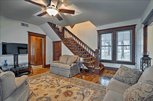 Cozy living room with a staircase, wooden accents, a TV, and comfortable seating on a patterned rug.