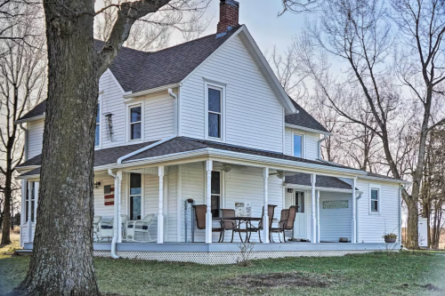 A charming white two-story house with a porch, surrounded by trees and a grassy yard.