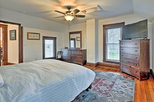 Cozy bedroom with a ceiling fan, wooden furniture, and large windows letting in natural light.