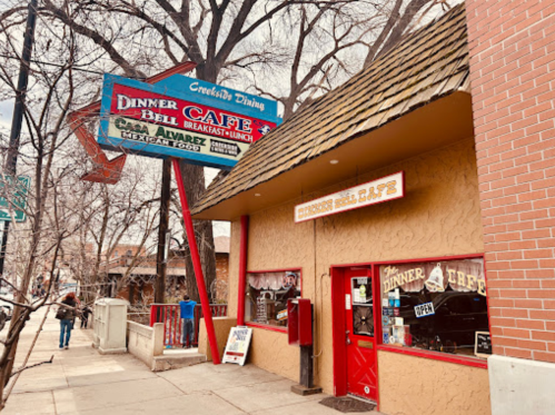A cozy café with a sign reading "Dinner Bell Café," featuring a rustic exterior and outdoor seating.