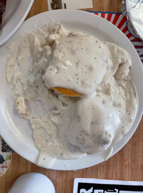 A plate with a biscuit covered in creamy sausage gravy, with some gravy spilled around the edges.